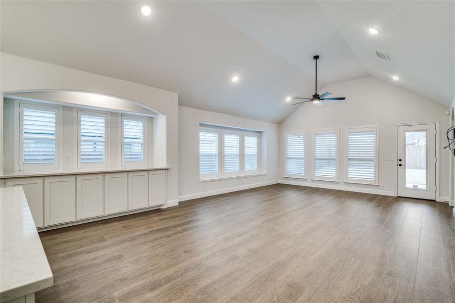 Unfurnished living room featuring plantation shutters, a fabulous buffet for entertaing, wood-type flooring, ceiling fan, and lofted ceiling