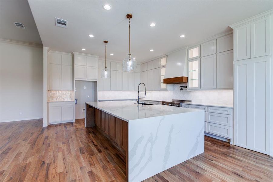 Kitchen with a large island, light stone countertops, hardwood / wood-style flooring, and white cabinetry