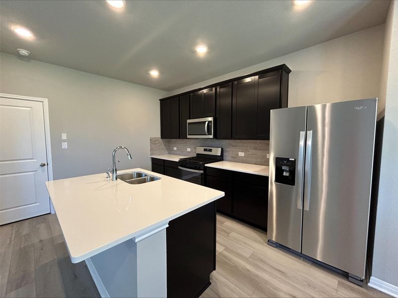 Kitchen featuring appliances with stainless steel finishes, dark cabinetry, a center island with sink, tasteful backsplash, and recessed lighting Kitchen featuring appliances with stainless steel finishes, dark cabinetry, a center island with sink, tasteful backsplash, and recessed lighting