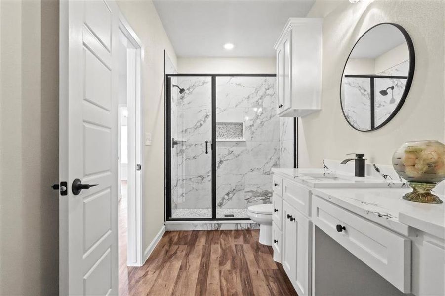 Bathroom featuring a marble finish shower, vanity, and dark wood-style flooring Bathroom featuring a marble finish shower, vanity, and dark wood-style flooring