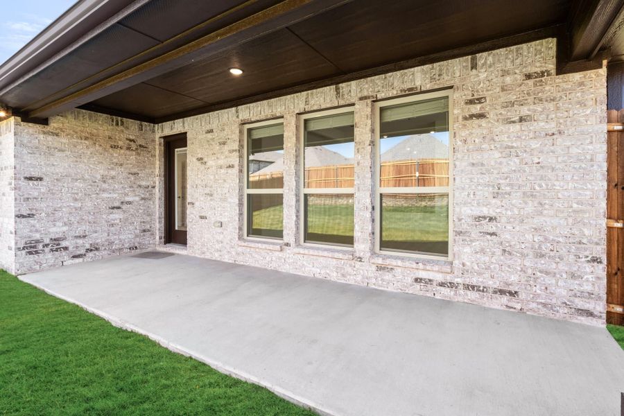 Covered back patio with concrete slab, light brick exterior, large windows, and wood ceiling with recessed lighting