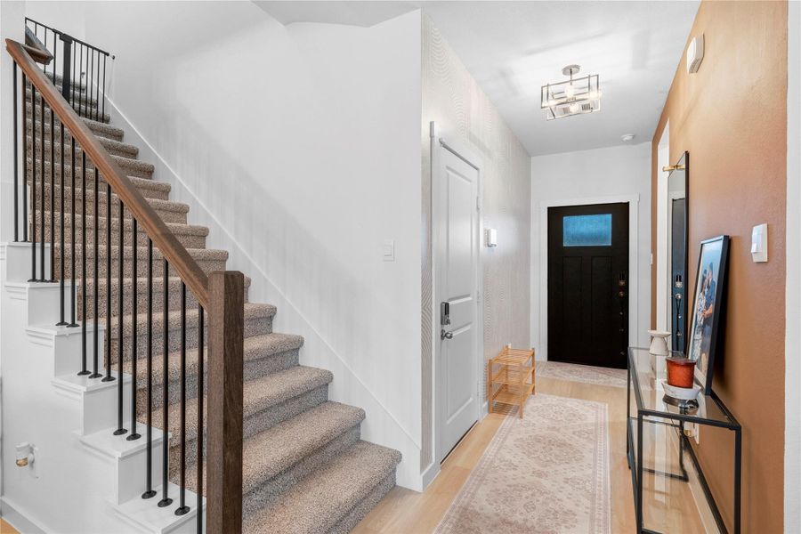 Another angle of the foyer reveals a carpeted staircase with dark railing, paired with a clean-lined hallway leading to the entry door. Another angle of the foyer reveals a carpeted staircase with dark railing, paired with a clean-lined hallway leading to the entry door.