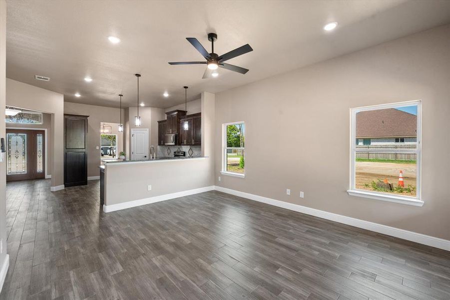 Open-concept living area featuring wood-finish flooring, recessed lighting, and a dark-toned ceiling fan. View from back of house facing kitchen.