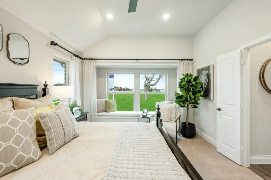 Bedroom with vaulted ceiling, window seat, ceiling fan, and large windows overlooking a green lawn