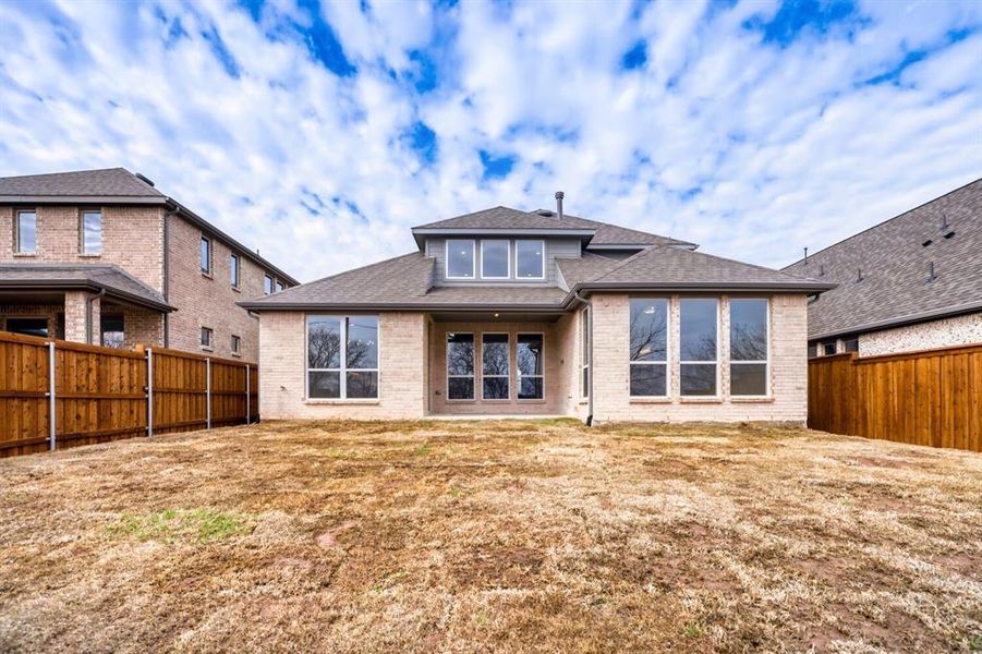 Back of house featuring brick siding, a fenced backyard, roof with shingles, and a patio area
