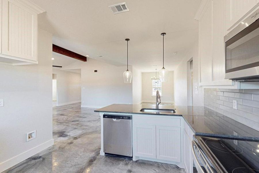 Kitchen featuring stainless steel appliances, a peninsula, a sink, visible vents, and decorative backsplash