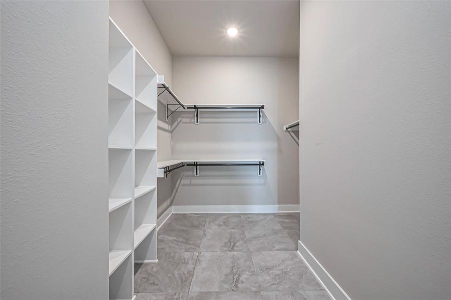 Discover a spacious walk-in closet with tile flooring, ample shelving, and hanging rods for perfect organization.