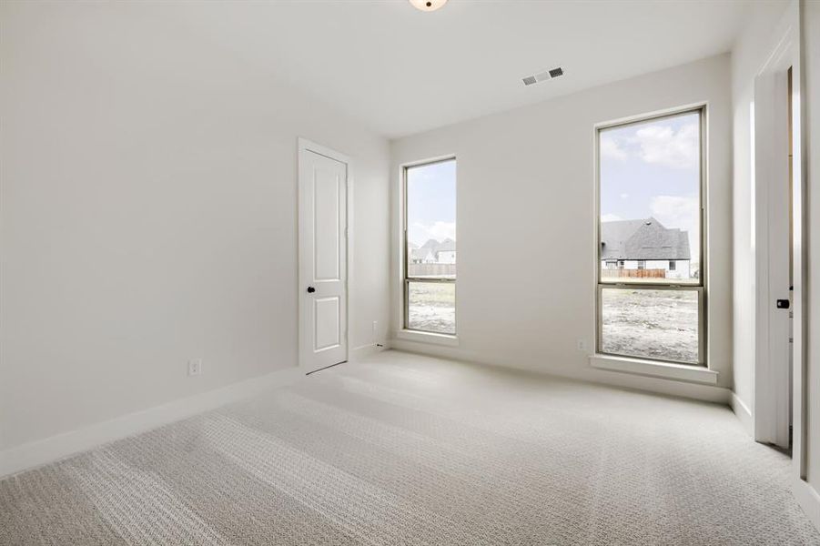 Carpeted room featuring two tall windows, white walls, and a white paneled door Carpeted room featuring two tall windows, white walls, and a white paneled door
