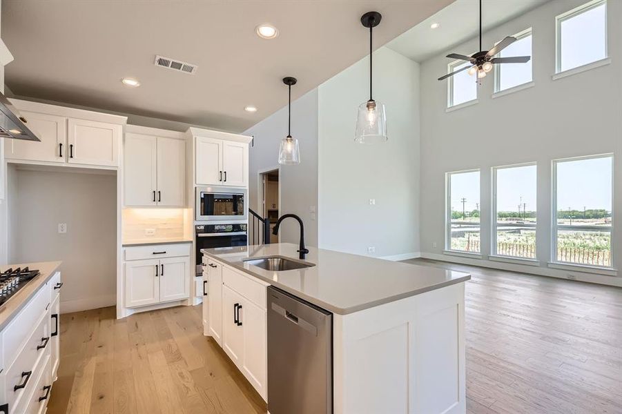 Kitchen featuring stainless steel appliances, a sink, a ceiling fan, light wood-type flooring, and hanging light fixtures Kitchen featuring stainless steel appliances, a sink, a ceiling fan, light wood-type flooring, and hanging light fixtures