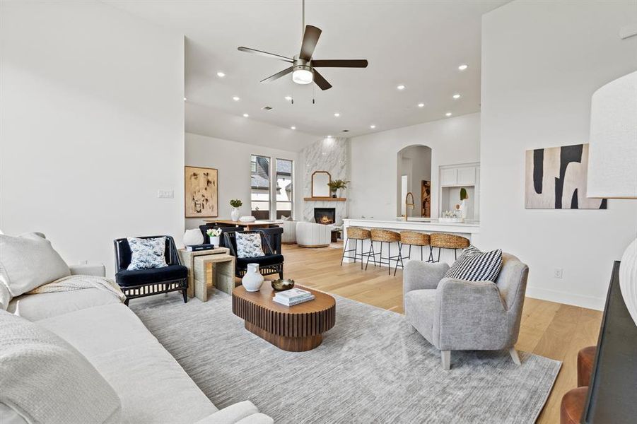 Living room with light wood-style flooring, arched walkways, a fireplace, recessed lighting, and ceiling fan