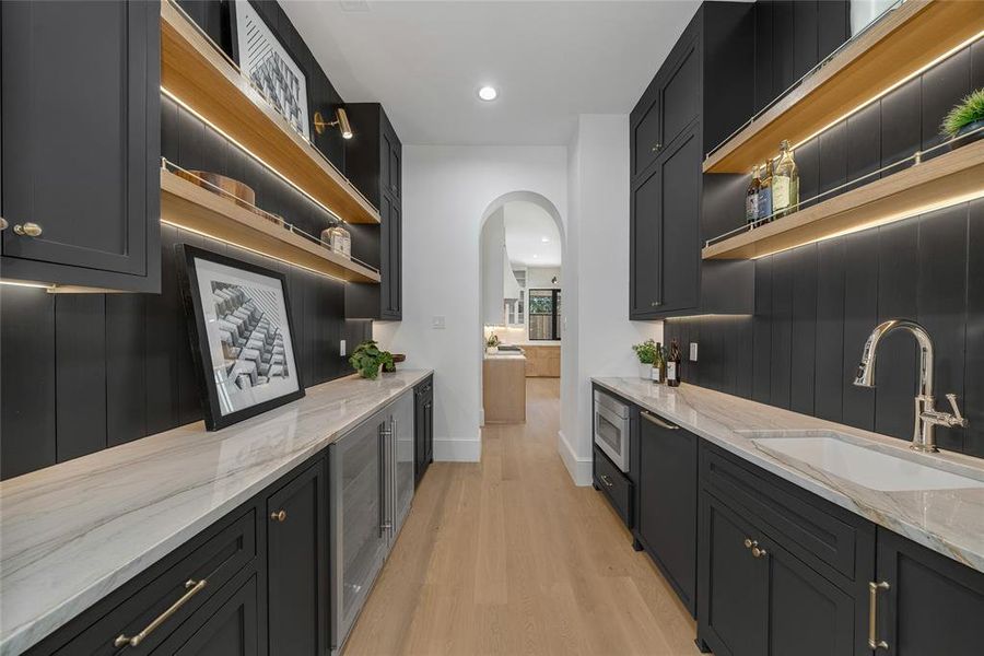 Contemporary butler's pantry featuring dark cabinetry, light wood-finish open shelving with integrated lighting, a built-in beverage refrigerator, and a stainless steel sink with a gooseneck faucet