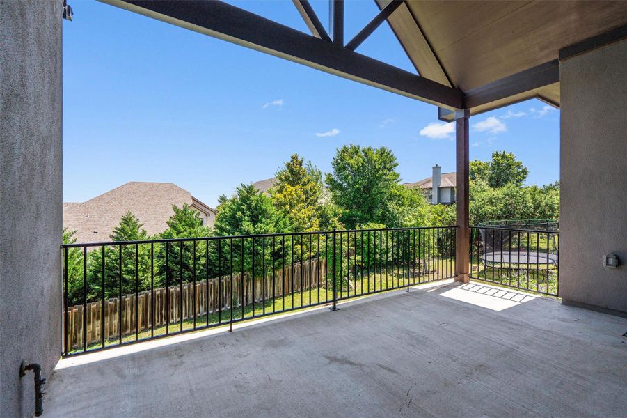Spacious covered balcony featuring a concrete surface, black iron railing, and exposed beam ceiling