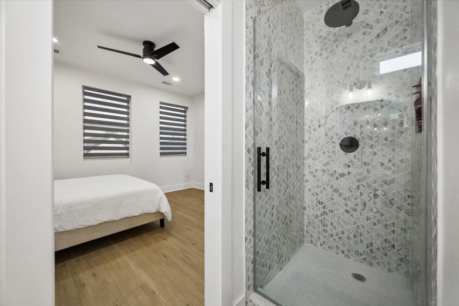 Primary suite with an adjoining ensuite bath featuring a spacious walk-in shower with floor-to-ceiling geometric tile, a frameless glass enclosure, rainfall showerhead, and modern matte-black fixtures. Primary suite with an adjoining ensuite bath featuring a spacious walk-in shower with floor-to-ceiling geometric tile, a frameless glass enclosure, rainfall showerhead, and modern matte-black fixtures.