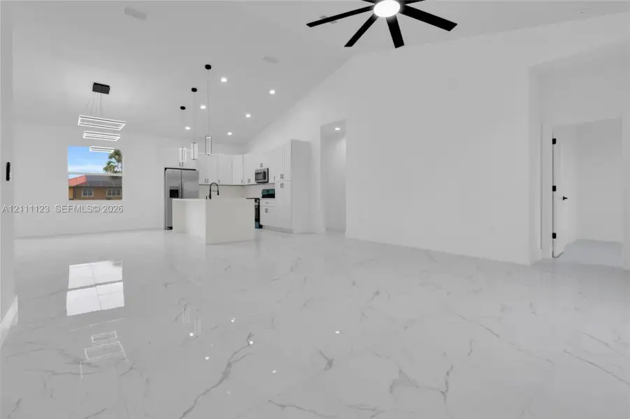 Open living area with cathedral ceiling, ceiling fan, and 32x32 polished Calacatta-style porcelain tile open to the kitchen.