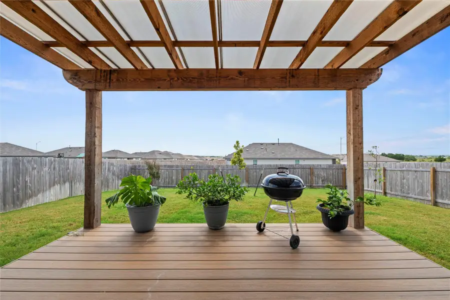 A spacious outdoor deck with a covered pergola offers an ideal setting for gatherings and enjoying the verdant backyard.