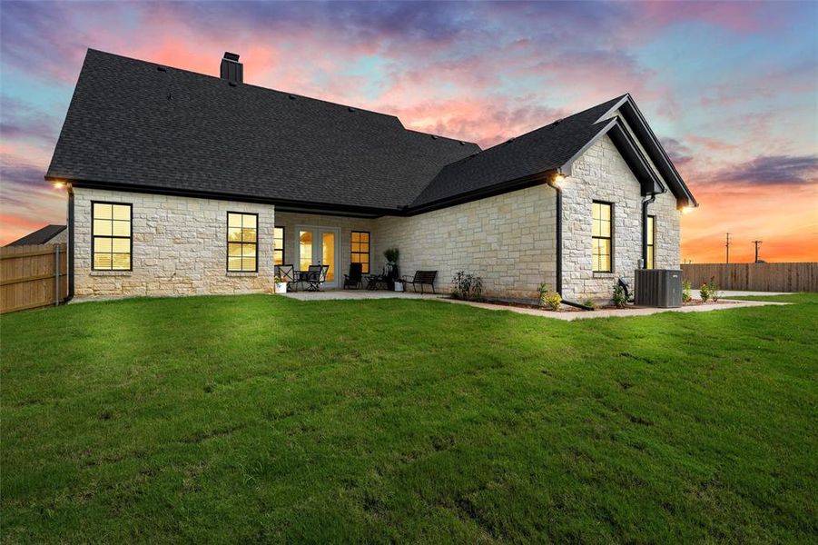 Back of property featuring stone siding, a chimney, a patio, and a shingled roof Back of property featuring stone siding, a chimney, a patio, and a shingled roof