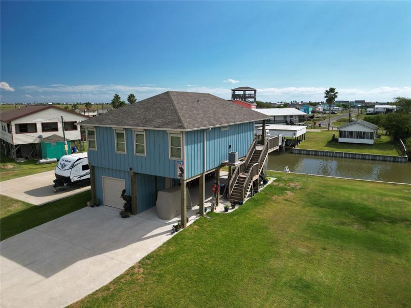 This elevated two-story home features a blue facade with a single garage and a spacious driveway. The open area underneath offers additional covered parking or storage space.