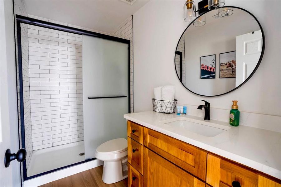 Well-appointed bathroom featuring a shower with white subway tile, a natural wood vanity with a white countertop, and a round mirror