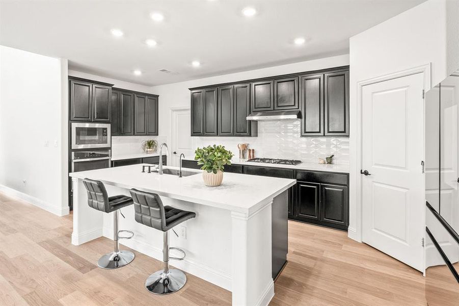 Kitchen featuring dark cabinetry, a breakfast bar area, a kitchen island with sink, tasteful backsplash, and recessed lighting