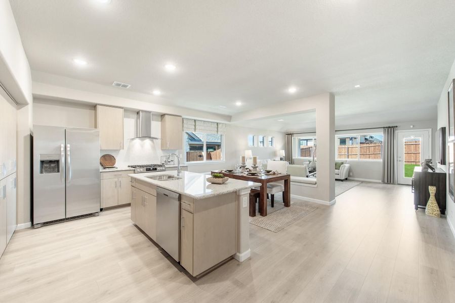 Open-concept kitchen with center island, stainless steel appliances, and light wood floors flowing into dining and living areas Open-concept kitchen with center island, stainless steel appliances, and light wood floors flowing into dining and living areas