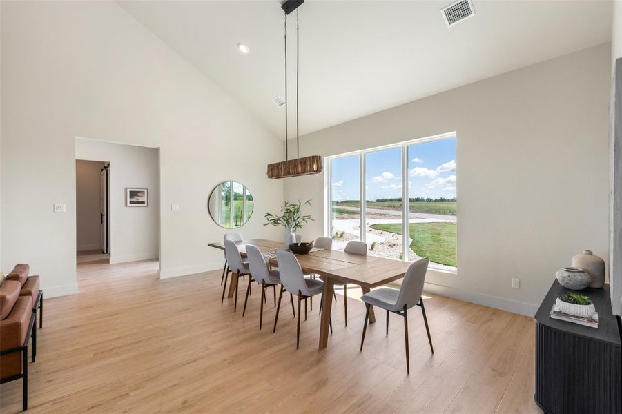 Dining space with high vaulted ceiling, light wood-type flooring, baseboards, a water view, and recessed lighting Dining space with high vaulted ceiling, light wood-type flooring, baseboards, a water view, and recessed lighting