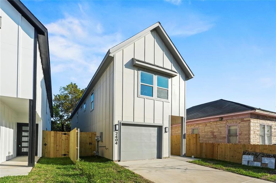 View of front of property with board and batten siding, a gate, an attached garage, and driveway