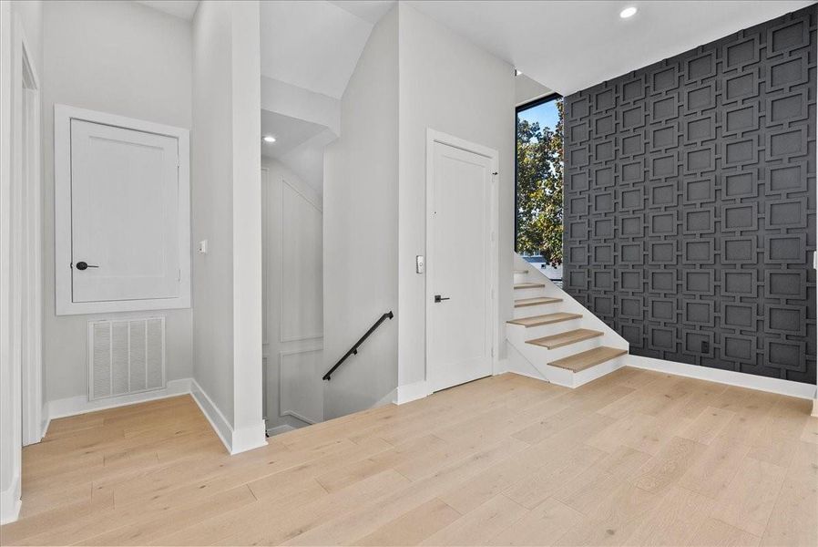 This photo showcases a modern, well-lit entryway with light wood flooring and a striking geometric accent wall. It features a staircase with wooden steps, sleek white walls, and contemporary doors, creating a clean and inviting atmosphere. This photo showcases a modern, well-lit entryway with light wood flooring and a striking geometric accent wall. It features a staircase with wooden steps, sleek white walls, and contemporary doors, creating a clean and inviting atmosphere.