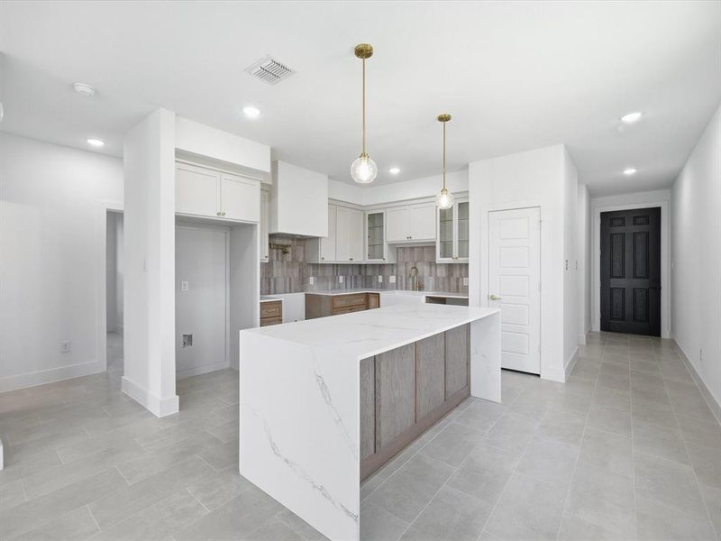 Kitchen featuring tasteful backsplash, glass insert cabinets, light stone counters, recessed lighting, and hanging light fixtures