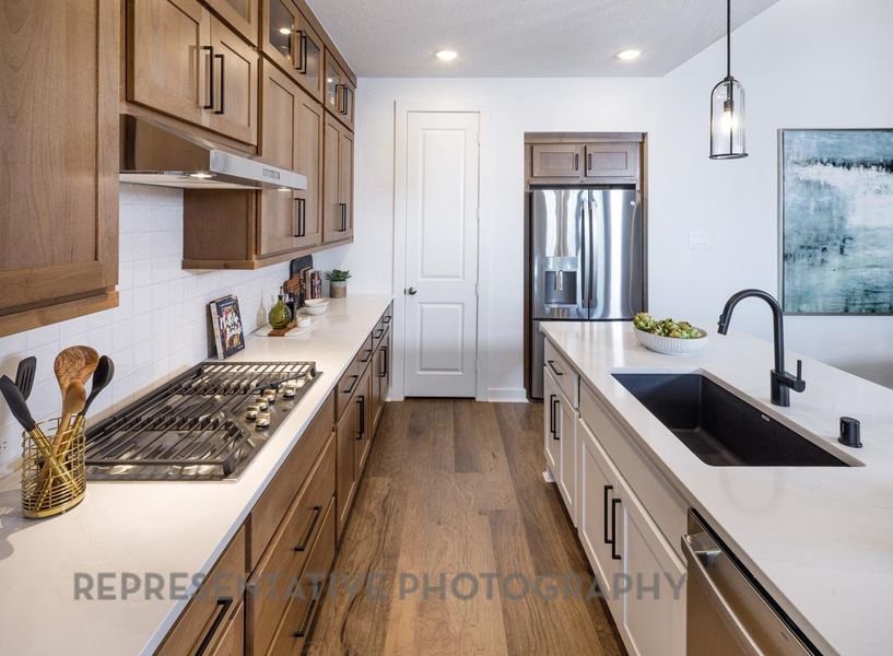 Kitchen featuring under cabinet range hood, stainless steel appliances, glass insert cabinets, dark wood-type flooring, and light countertops