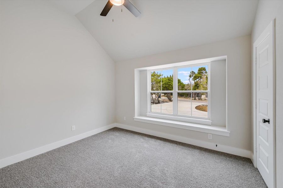 Carpeted spare room featuring baseboards, vaulted ceiling, and a ceiling fan