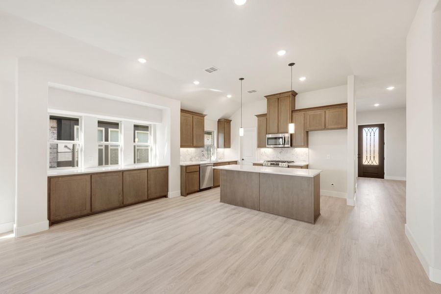 Open kitchen with brown wood cabinets, center island, pendant lights, and light hardwood floors