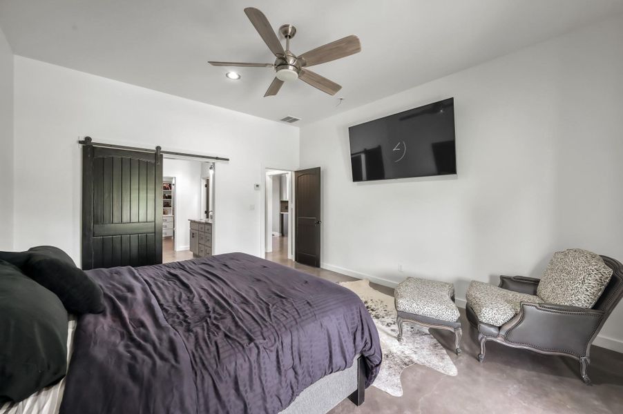 This bedroom features a sleek, modern design with a ceiling fan, mounted TV, and a sliding barn door leading to a spacious en-suite bathroom.