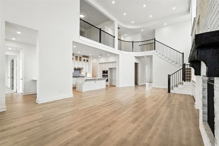 Unfurnished living room with recessed lighting, light wood-style floors, a high ceiling, a large fireplace, and stairway Unfurnished living room with recessed lighting, light wood-style floors, a high ceiling, a large fireplace, and stairway