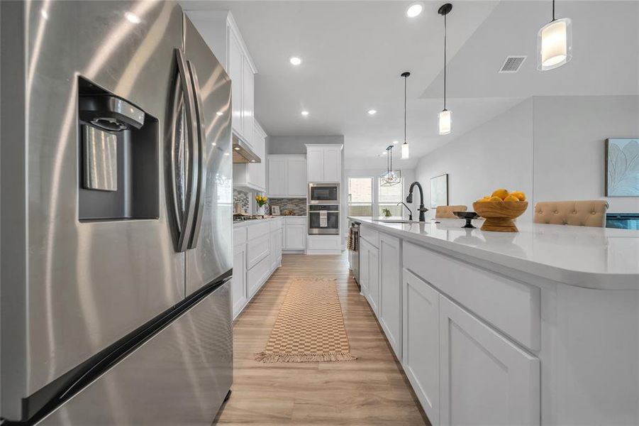 Kitchen featuring appliances with stainless steel finishes, white cabinetry, pendant lighting, light wood finished floors, and recessed lighting Kitchen featuring appliances with stainless steel finishes, white cabinetry, pendant lighting, light wood finished floors, and recessed lighting