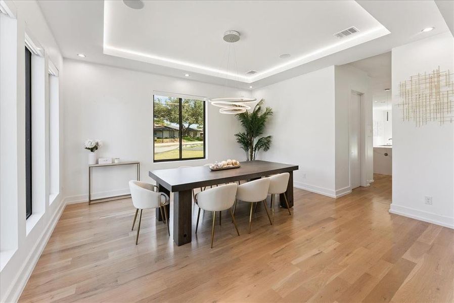 Dining space with light wood-type flooring, a raised ceiling, recessed lighting, and a chandelier