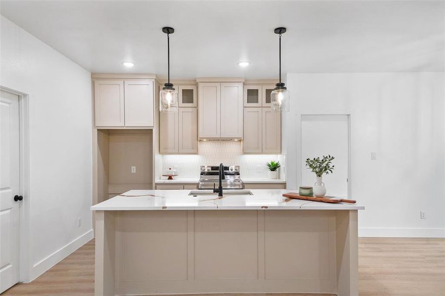 Contemporary kitchen featuring a spacious island with a light-toned countertop, pendant lighting, shaker-style cabinetry, and wood-finish flooring Contemporary kitchen featuring a spacious island with a light-toned countertop, pendant lighting, shaker-style cabinetry, and wood-finish flooring