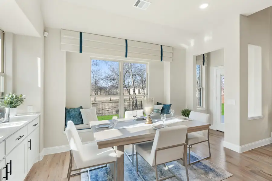 Dining area with built-in bench seating, white chairs, gray table, and large window with blue Roman shades Dining area with built-in bench seating, white chairs, gray table, and large window with blue Roman shades