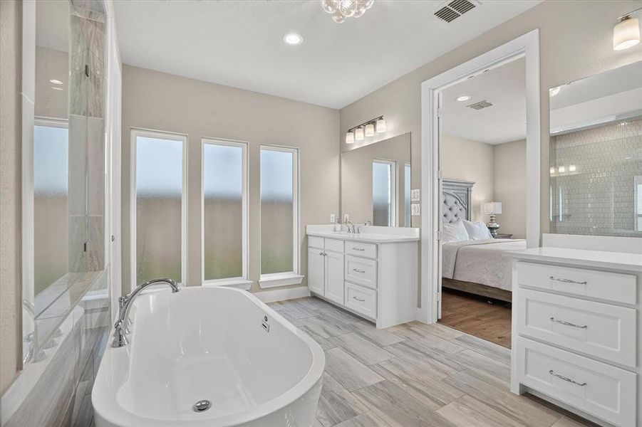 Freestanding soaking tub with chrome fixtures, three vertical privacy windows, and wood-finish flooring Freestanding soaking tub with chrome fixtures, three vertical privacy windows, and wood-finish flooring