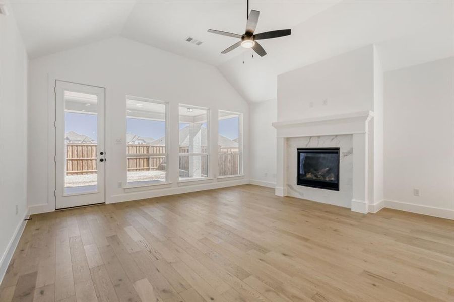 Unfurnished living room with ceiling fan, light wood-style floors, a high end fireplace, and a high ceiling