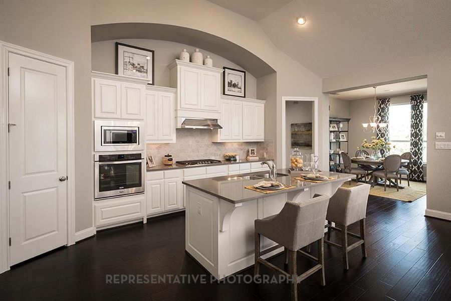 Kitchen featuring a kitchen breakfast bar, white cabinetry, appliances with stainless steel finishes, tasteful backsplash, and vaulted ceiling Kitchen featuring a kitchen breakfast bar, white cabinetry, appliances with stainless steel finishes, tasteful backsplash, and vaulted ceiling