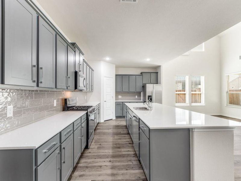 Kitchen with gray cabinetry, appliances with stainless steel finishes, light wood-type flooring, decorative backsplash, and a kitchen island with sink