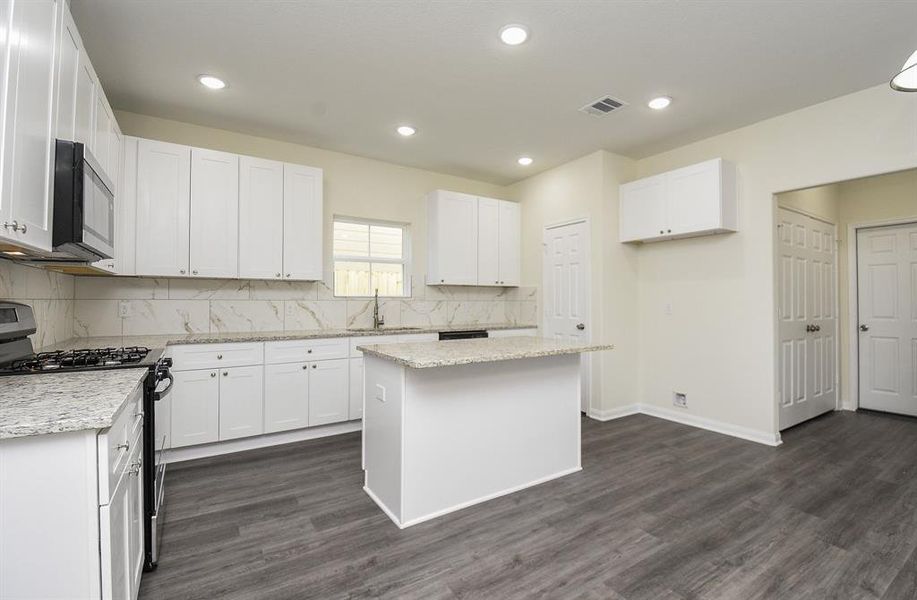 Modern kitchen interior with white cabinets, granite countertops, stainless steel appliances, and grey wood flooring.