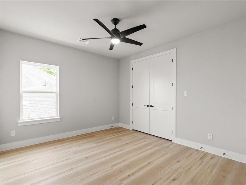 Interior room featuring light wood-finish flooring, a contemporary black ceiling fan with integrated lighting, white trim work, and a double-door closet with black hardware Interior room featuring light wood-finish flooring, a contemporary black ceiling fan with integrated lighting, white trim work, and a double-door closet with black hardware