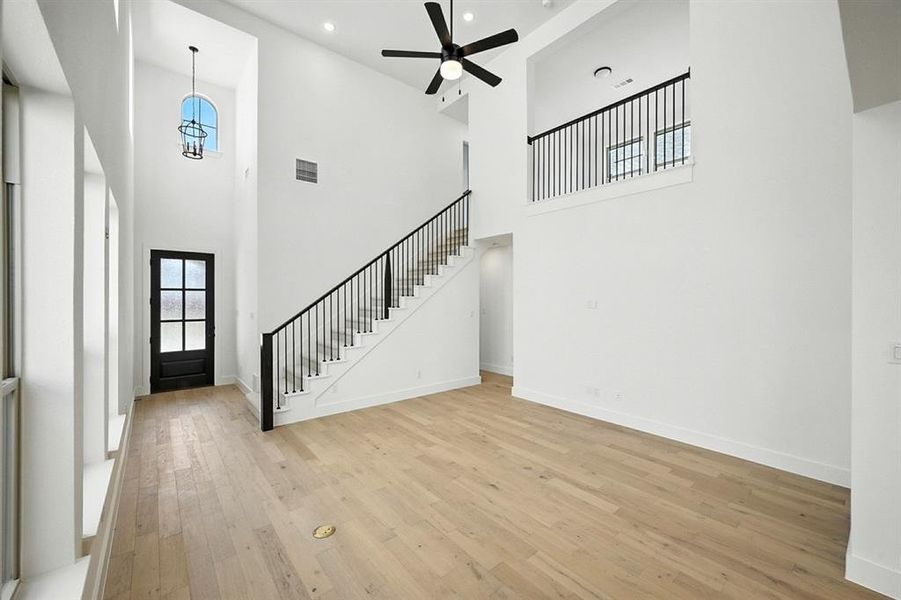 Unfurnished living room with light wood-style floors, a high ceiling, recessed lighting, stairs, and a ceiling fan Unfurnished living room with light wood-style floors, a high ceiling, recessed lighting, stairs, and a ceiling fan