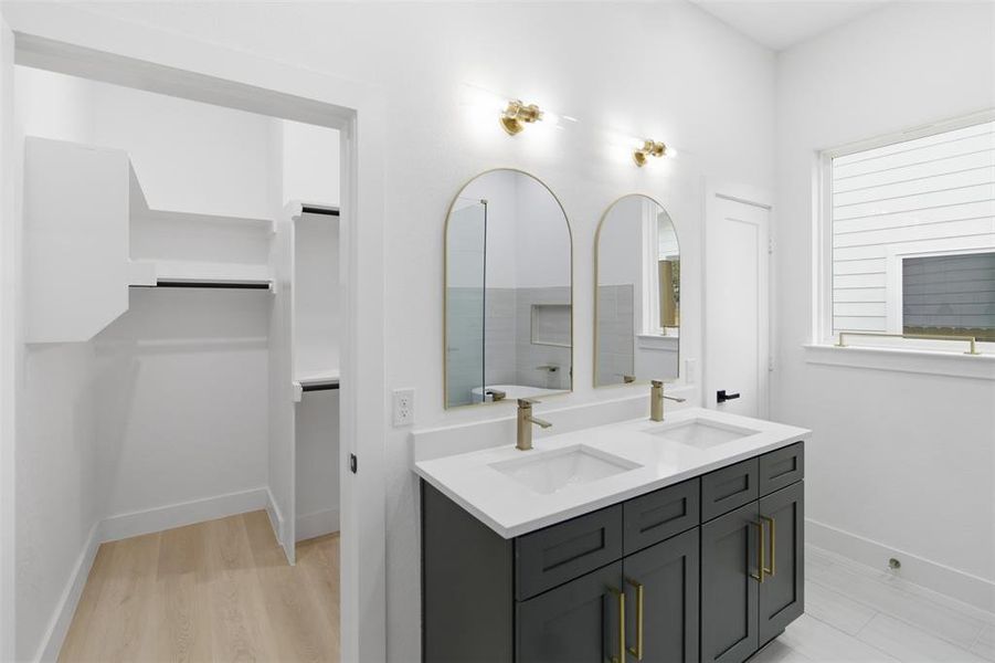 Full bath with a spacious closet, double vanity, and light wood-type flooring