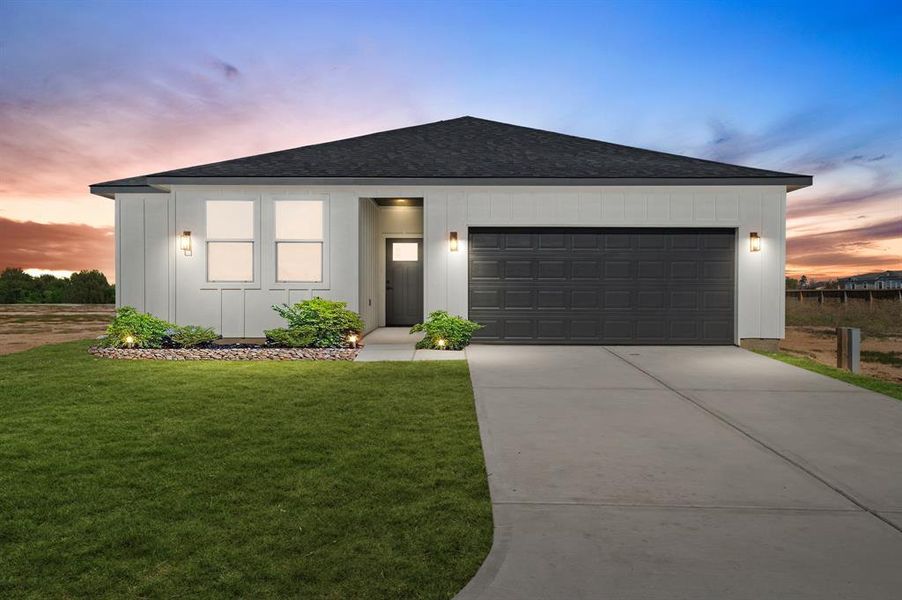 This is a modern single-story home featuring clean lines, a two-car garage, and a neatly landscaped entryway, captured at dusk with a beautiful sunset in the background.