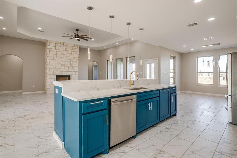 Kitchen featuring appliances with stainless steel finishes, blue cabinets, decorative light fixtures, a fireplace, and an island with sink