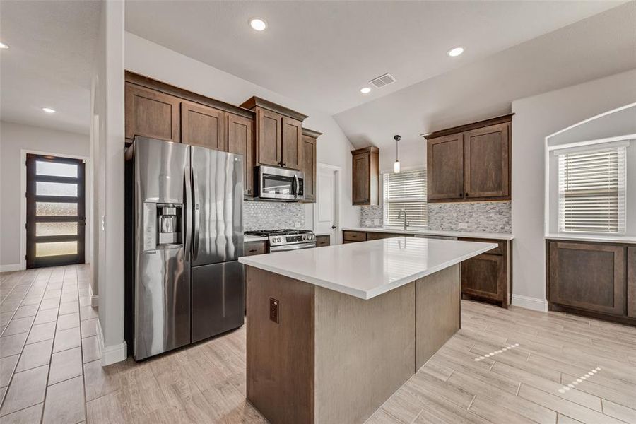 Kitchen featuring appliances with stainless steel finishes, a center island, lofted ceiling, backsplash, and light wood-style floors Kitchen featuring appliances with stainless steel finishes, a center island, lofted ceiling, backsplash, and light wood-style floors