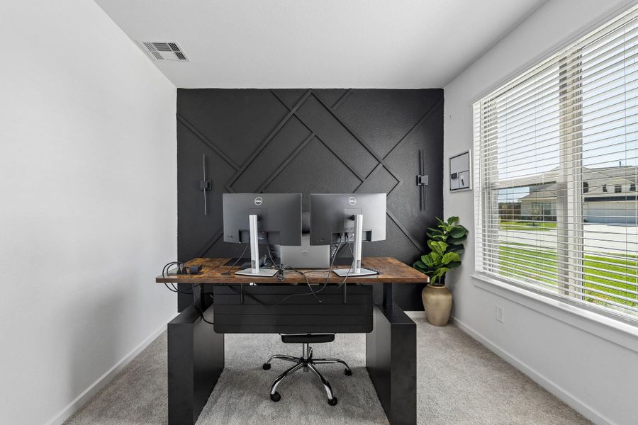 Located behind french doors at the front of the home, this workspace features a high-contrast accent wall, neutral carpeting, and insulated/Low-E windows. Modern lighting and high ceilings enhance the functional layout.