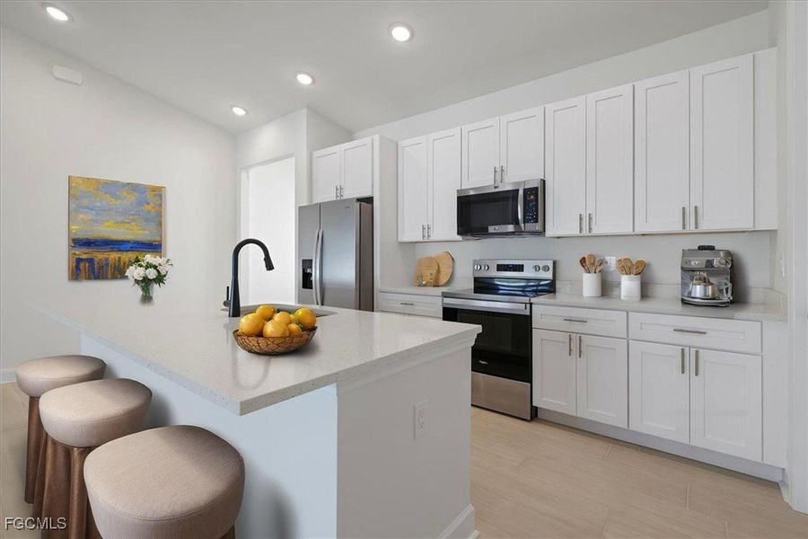 Kitchen featuring appliances with stainless steel finishes, an island with sink, white cabinets, light stone counters, and a kitchen bar Kitchen featuring appliances with stainless steel finishes, an island with sink, white cabinets, light stone counters, and a kitchen bar